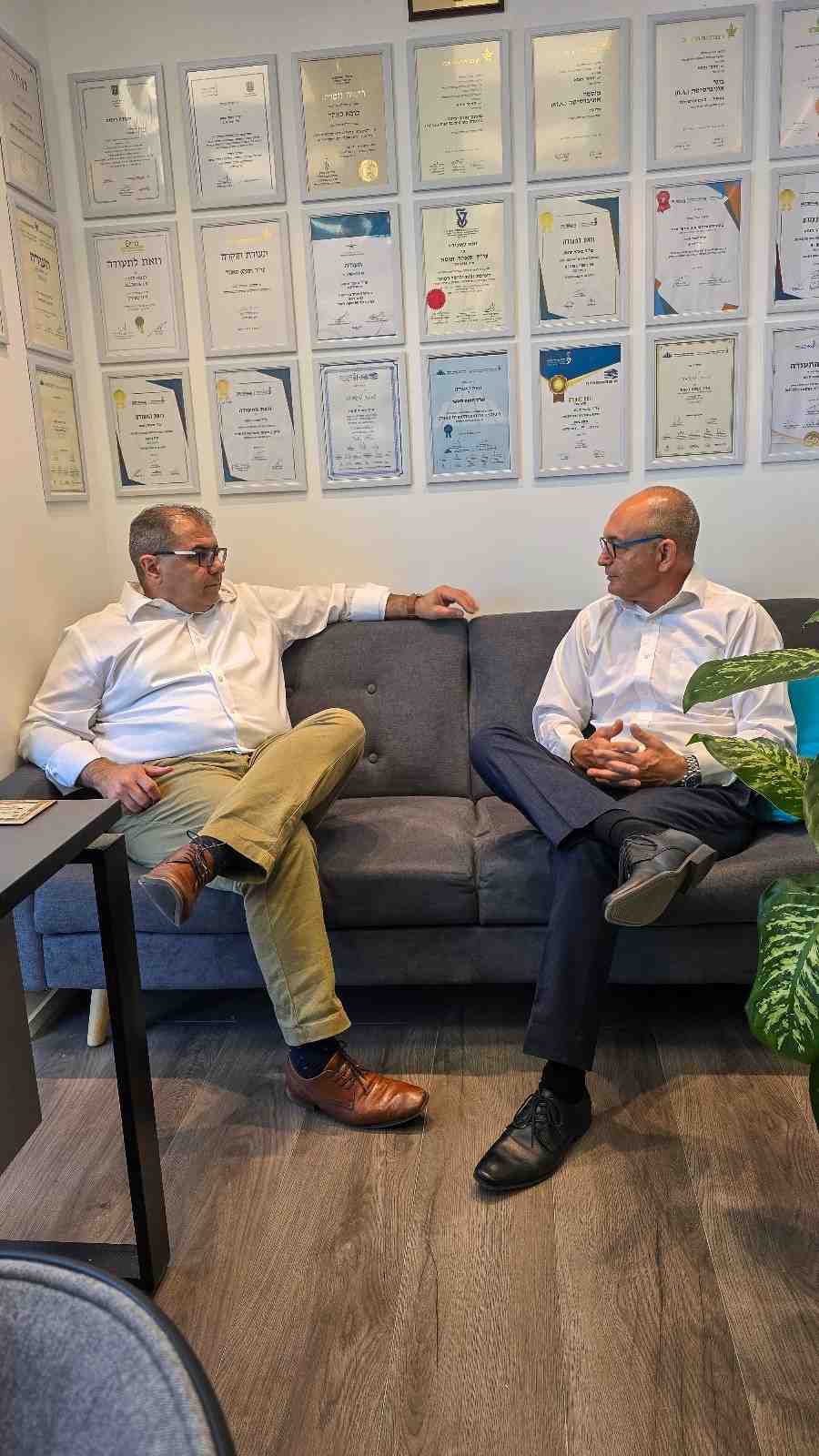 עורך דין רשלנות רפואית מייעץ ללקוח במשרד על רקע קיר תעודות הסמכה.